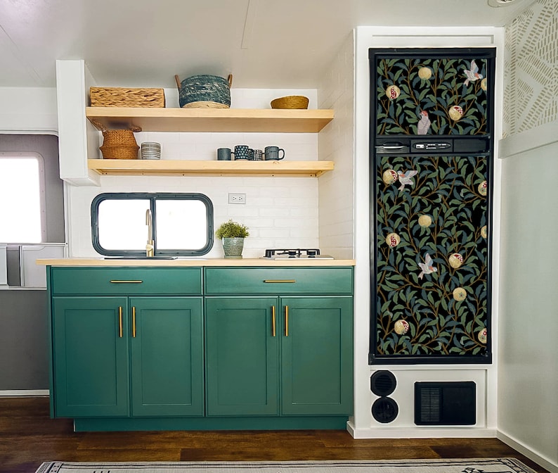 May include: A kitchen with green cabinets and a black refrigerator with a floral print. The refrigerator has a black door with a floral pattern and a black handle. The cabinets have gold handles. The kitchen has a white countertop and a white backsplash.