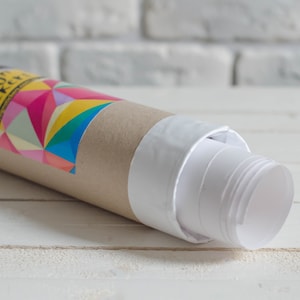 K&ouml;nnte beinhalten: Ein aufgerolltes Poster mit einer wei&szlig;en R&uuml;ckseite und einer braunen Pappr&ouml;hre. Die R&ouml;hre hat ein buntes geometrisches Design und den Text "Design Stickery" aufgedruckt.