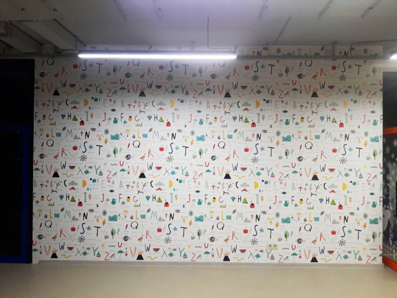 May include: A white wall with a repeating pattern of colorful letters, symbols, and illustrations. The letters are in a variety of fonts and sizes, and the symbols and illustrations are abstract and whimsical.