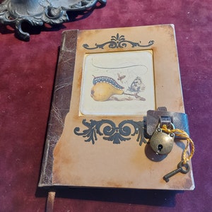 May include: A brown leather-bound journal with a lock and key. The cover features a decorative design and a vintage illustration of a pear with a caterpillar and butterflies.