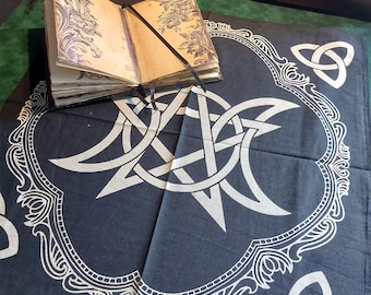 May include: Black cotton tapestry with a white triple moon and pentagram design. The tapestry has a white ornate border with three white triquetra knots in each corner.