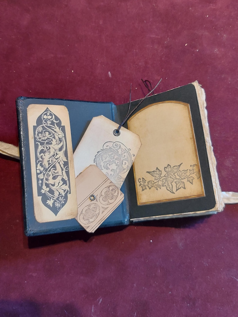 Puede incluir: Un peque&ntilde;o diario encuadernado en cuero negro con un dise&ntilde;o floral decorativo en la portada. El diario est&aacute; abierto para revelar una p&aacute;gina en blanco con un borde decorativo. Hay tres etiquetas en blanco con dise&ntilde;os florales adjuntas al diario.