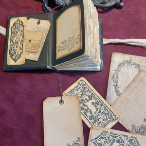 Puede incluir: Un diario encuadernado en cuero negro con p&aacute;ginas en blanco y etiquetas decorativas. El diario tiene una est&eacute;tica vintage y est&aacute; adornado con intrincados dise&ntilde;os florales. Las etiquetas son de papel y tienen un dise&ntilde;o floral similar.