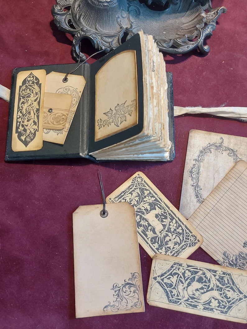 Puede incluir: Un diario encuadernado en cuero negro con p&aacute;ginas en blanco y etiquetas decorativas. El diario tiene una est&eacute;tica vintage y est&aacute; adornado con intrincados dise&ntilde;os florales. Las etiquetas son de papel y tienen un dise&ntilde;o floral similar.