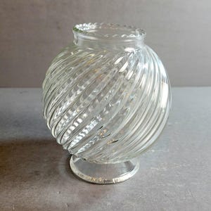 May include: A clear glass globe lampshade featuring a spherical body with a distinct diagonal swirl pattern. The shade has a circular opening at the top with a scalloped edge and a smaller circular base, designed for attachment to a light fixture.
