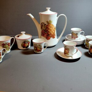 May include: A white porcelain tea set with a fruit design. The set includes a teapot, creamer, sugar bowl, and four cups and saucers.