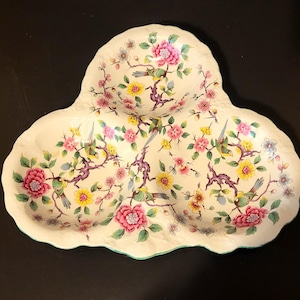May include: A white ceramic serving dish with three sections, featuring a floral pattern with pink, yellow, and green flowers and birds. The dish has a scalloped edge.