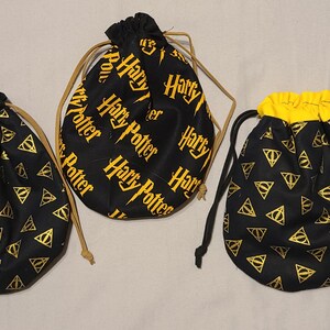 May include: Three black drawstring bags with gold accents. One bag features the words "Harry Potter" in gold, while the other two have a repeating gold symbol pattern. The bags have drawstrings for closure.