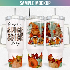 May include: White stainless steel tumbler with a handle. The tumbler features a autumnal design with gnomes, pumpkins, and leaves. The text "Pumpkin Spice Spice Baby" is printed on the tumbler.