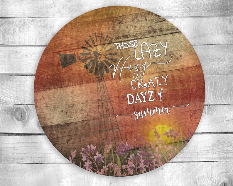 May include: A round wooden sign with a rustic woodgrain background. The sign features a silhouette of a windmill with a sunset in the background. The text on the sign reads "Those Lazy Hazy Crazy Dayz of Summer".