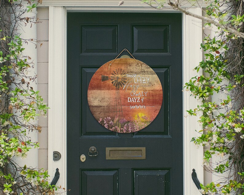 May include: A round wooden sign with a rustic, weathered look. The sign features a colourful sunset background with a windmill silhouette and the text "Those Lazy, Hazy, Crazy Days of Summer".