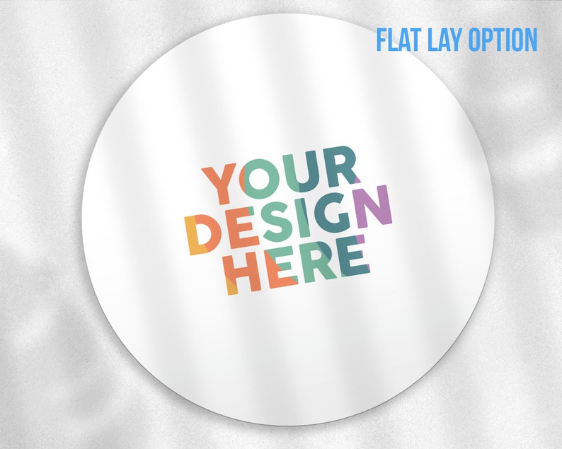 May include: White round sticker with the text "YOUR DESIGN HERE" in colourful letters. The text is arranged in a diagonal pattern with the word "YOUR" at the top and the word "HERE" at the bottom.