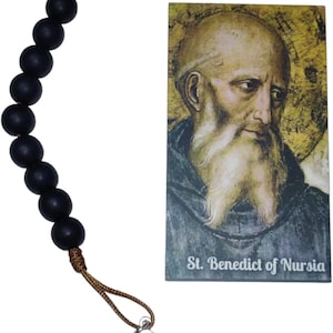 May include: A rosary with black beads, a silver crucifix, and a St. Benedict medal. A card with an image of St. Benedict of Nursia is also included. The rosary is made with a brown cord.