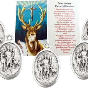 May include: Oval silver-toned Saint Hubert medals with a depiction of Saint Hubert, a deer, and a dog. A card with text about Saint Hubert, the patron saint of hunters, is also visible.