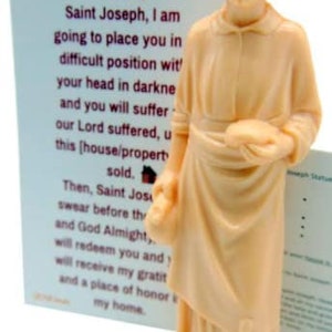 May include: A beige figurine of Saint Joseph holding a small wooden house. The figurine is standing on a beige base. The figurine is accompanied by a card with a prayer to Saint Joseph for help selling a house.