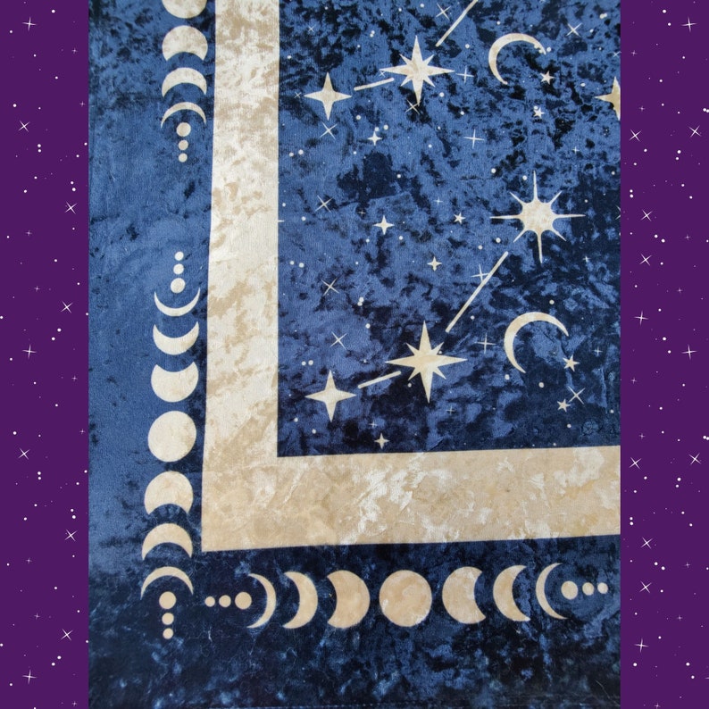 May include: A navy blue velvet tapestry with a celestial design. The tapestry features a cream-colored border and accents, with a pattern of stars, crescent moons, and phases of the moon. The background is a deep blue color.