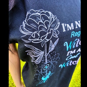 May include: Black t-shirt with a white floral design and the text "I'm Not a Regular Witch, I'm a Cool Witch" in rainbow colors.