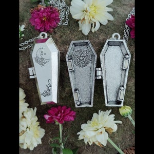 May include: Three silver coffin-shaped pendant necklaces with a pentagram and moon design. The pendants are open and have a hinged lid.