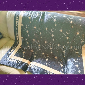 May include: A dark teal blanket with a celestial design featuring gold stars, crescent moons, and phases of the moon. The blanket has a soft, velvety texture and a cream-colored border. The text "ImaginedByNeil.etsy.com" is visible.