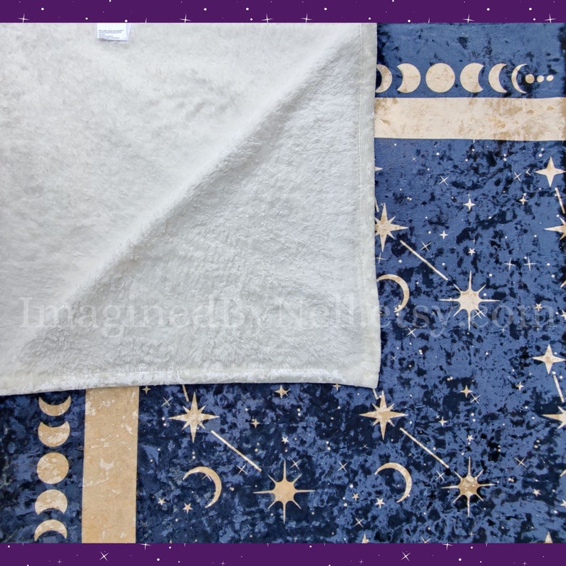 May include: A navy blue celestial-themed blanket with a soft, cream-colored underside. The patterned side features gold moons, stars, and constellations. The blanket is made of a plush, velvety material, perfect for cozy nights.