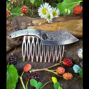 May include: A silver comb with a knife blade attached to the top. The comb has 12 teeth and is surrounded by green leaves and black berries.