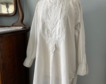May include: A white, long-sleeved shirt with a high collar and a decorative lace trim. The shirt has a pleated front and a button closure at the neck.