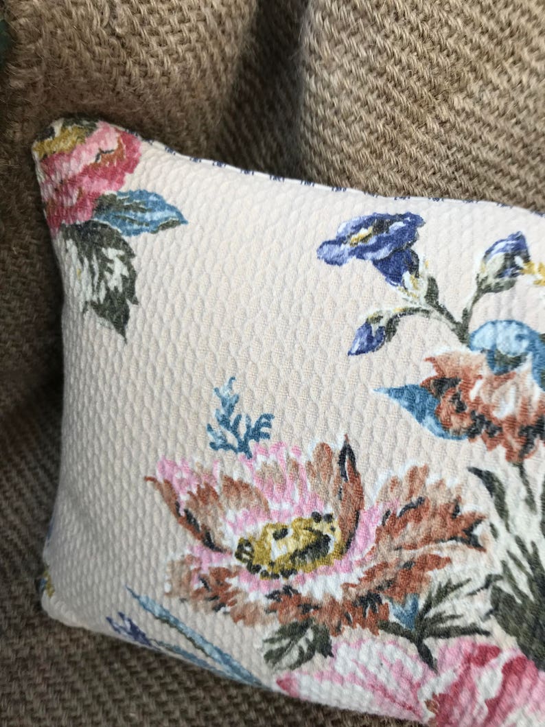 May include: A beige pillow with a floral pattern featuring pink, blue, and brown flowers. The pillow has a textured surface.