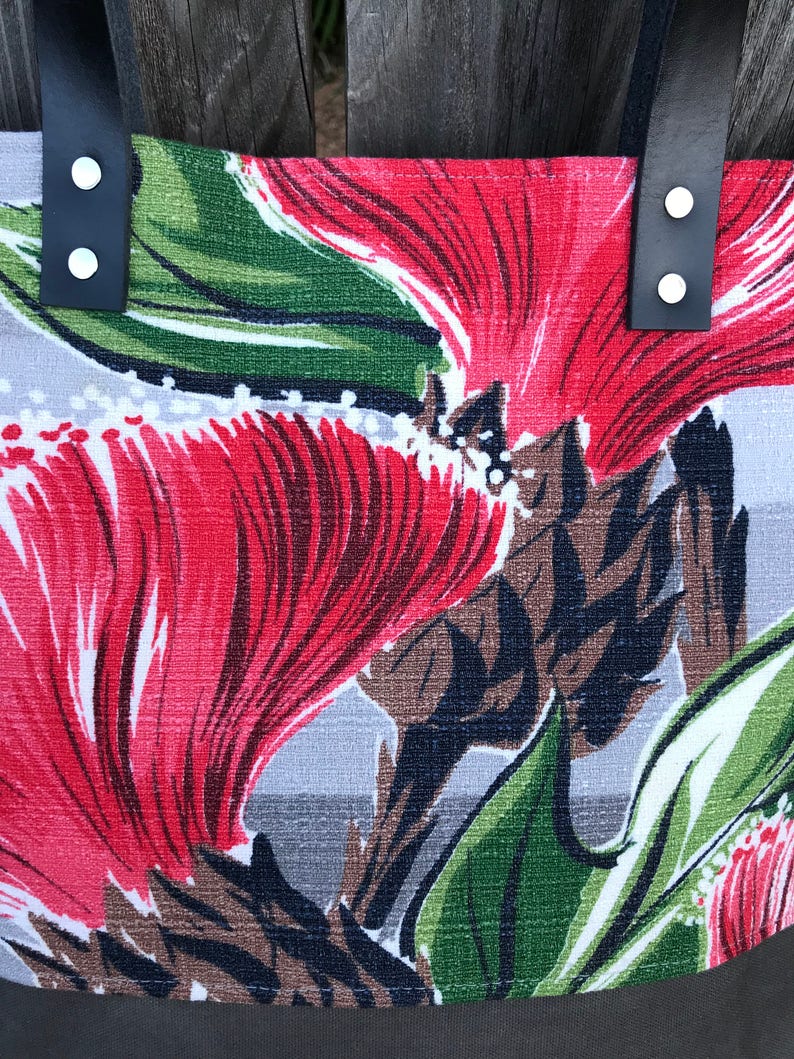 May include: A gray tote bag with red and green floral print. The bag has black leather straps with silver metal rivets.
