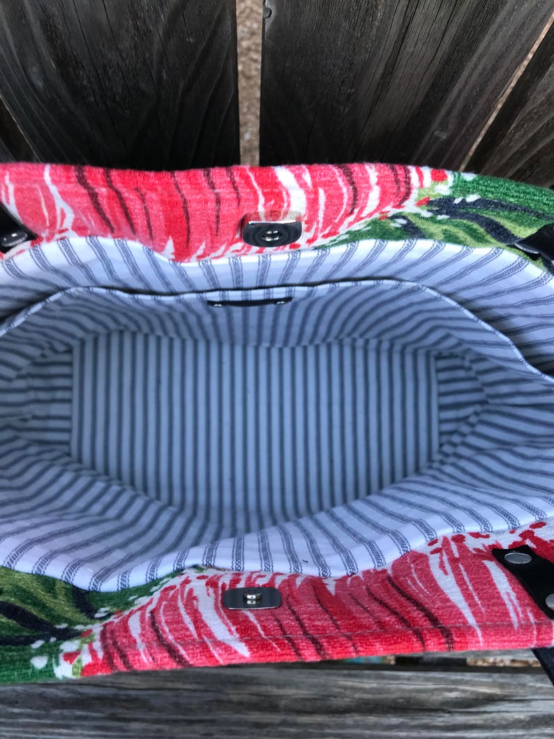 May include: A red and green floral tote bag with a striped fabric lining. The bag has two silver metal snaps and a black leather handle.