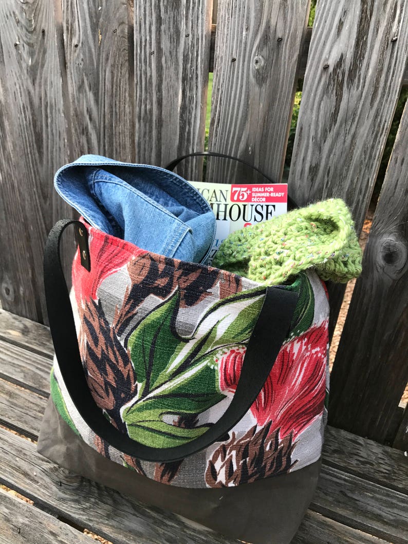 May include: A floral tote bag with black straps. The bag is filled with a blue denim shirt, a green crocheted hat, and a magazine titled "American House".