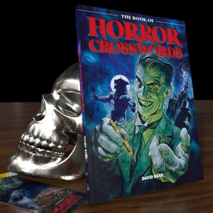 Peut inclure: Un livre intitulé "The Book of Horror Crosswords" avec un monstre à la peau verte sur la couverture tenant un crayon. Le monstre a un sourire sinistre et est entouré d'un loup-garou et d'une maison hantée. Le livre est de David Read.