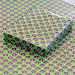 Könnte beinhalten: Eine Geschenkbox mit grünem und violettem Muster mit einem sich wiederholenden geometrischen Design. Die Box ist in Papier mit einem Muster aus überlappenden Kreisen verpackt.