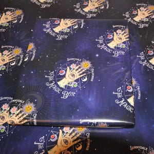 May include: A blue and black wrapping paper with a repeating pattern of a hand with an eye in the palm, surrounded by a circle, stars, and the text "The Magic Box" and "Sunnydale, California".