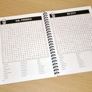 May include: A black and white word search puzzle book with a skull design on the cover. The book is open to a page with the title "Dr. Phibes" and a word search puzzle. The opposite page has the title "Buffy" and a word search puzzle.