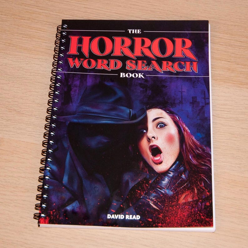 May include: The cover of a spiral bound book titled "The Horror Word Search Book" by David Read. The cover features a dark, shadowy figure with a wide-brimmed hat, holding a woman with a terrified expression. The background is a dark purple with a graveyard.