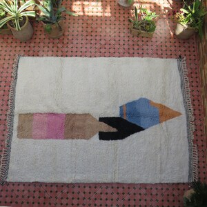 May include: A white rug with a geometric design in pink, brown, black, blue, and orange. The design resembles a stylized rocket ship.