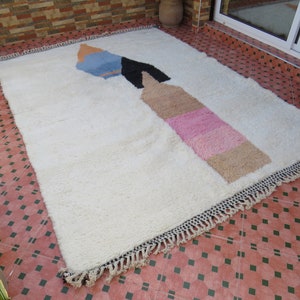 May include: A white shag rug with a colorful abstract design. The design features a large, geometric shape with shades of blue, pink, and brown.