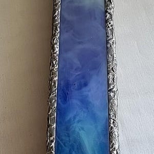 May include: A rectangular stained glass panel with a blue colour gradient. The glass is framed in a textured, silver-coloured metal. The bottom section is clear glass.