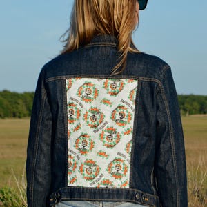 May include: Dark wash denim jacket with a rectangular patch on the back featuring a floral and skull design. The patch has the words "Grateful Dead" printed on it. The jacket has a classic button-up design.