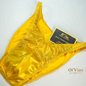 May include: A gold metallic swimsuit bottom with a shiny finish. The swimsuit is labeled "Ol'Viaz DESIGN CORPORATION OLGA VIAZMETINOVA".