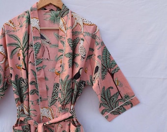 Peut inclure: Une robe en coton rose avec une bordure blanche et un imprimé jungle représentant des léopards, des oiseaux et des palmiers. La robe a une ceinture à nouer et des poches.