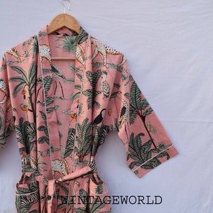 May include: A pink cotton robe with a white trim and a jungle print featuring leopards, birds, and palm trees. The robe has a tie belt and pockets.