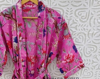 Peut inclure: Une robe en coton rose à imprimé floral avec des oiseaux et des feuilles. La robe est bordée de blanc et possède une ceinture assortie.