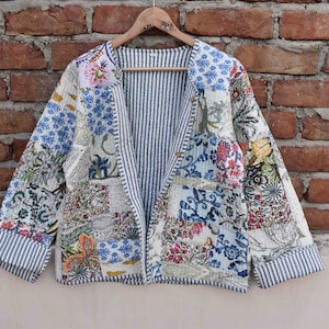 May include: A white quilted jacket with a blue and white striped lining. The jacket is made of patchwork fabric with floral patterns in shades of blue, pink, green, and yellow.