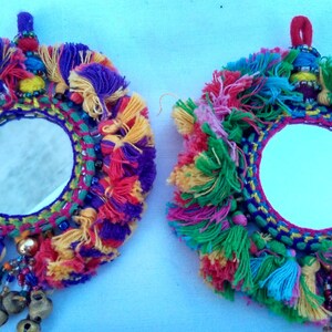 May include: Two round mirrors with colorful yarn tassels and beads. The mirrors are surrounded by a woven frame with a variety of colors, including red, blue, green, yellow, and purple. The mirrors are hanging from a string with a tassel.