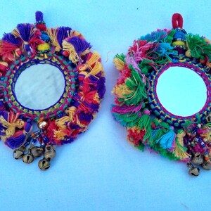 May include: Two round mirrors with colorful yarn tassels and bells hanging from the bottom. The mirrors are surrounded by a colorful embroidered border.