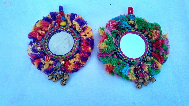 May include: Two round mirrors with colorful yarn tassels and bells hanging from the bottom. The mirrors are surrounded by a colorful embroidered border.