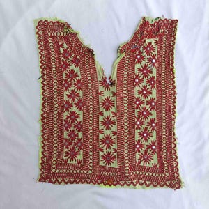 May include: A pale yellow sleeveless tunic top featuring dense red embroidery in floral and geometric patterns. The garment is embellished with small circular mirrors integrated into the center of the red floral motifs and has a deep V-neckline.