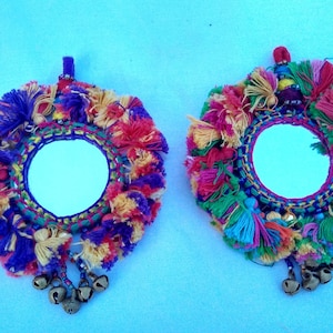May include: Two round mirrors with colorful yarn tassels and bells hanging from the bottom. The mirrors are surrounded by a colorful yarn fringe.