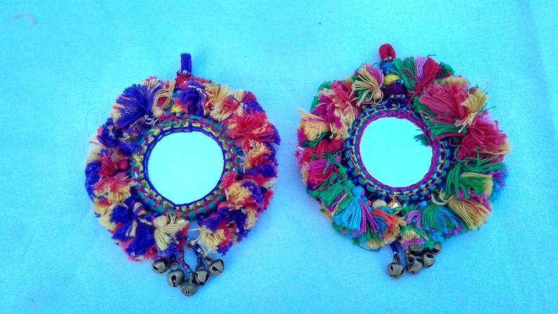 May include: Two round mirrors with colorful yarn tassels and bells hanging from the bottom. The mirrors are surrounded by a colorful yarn fringe.